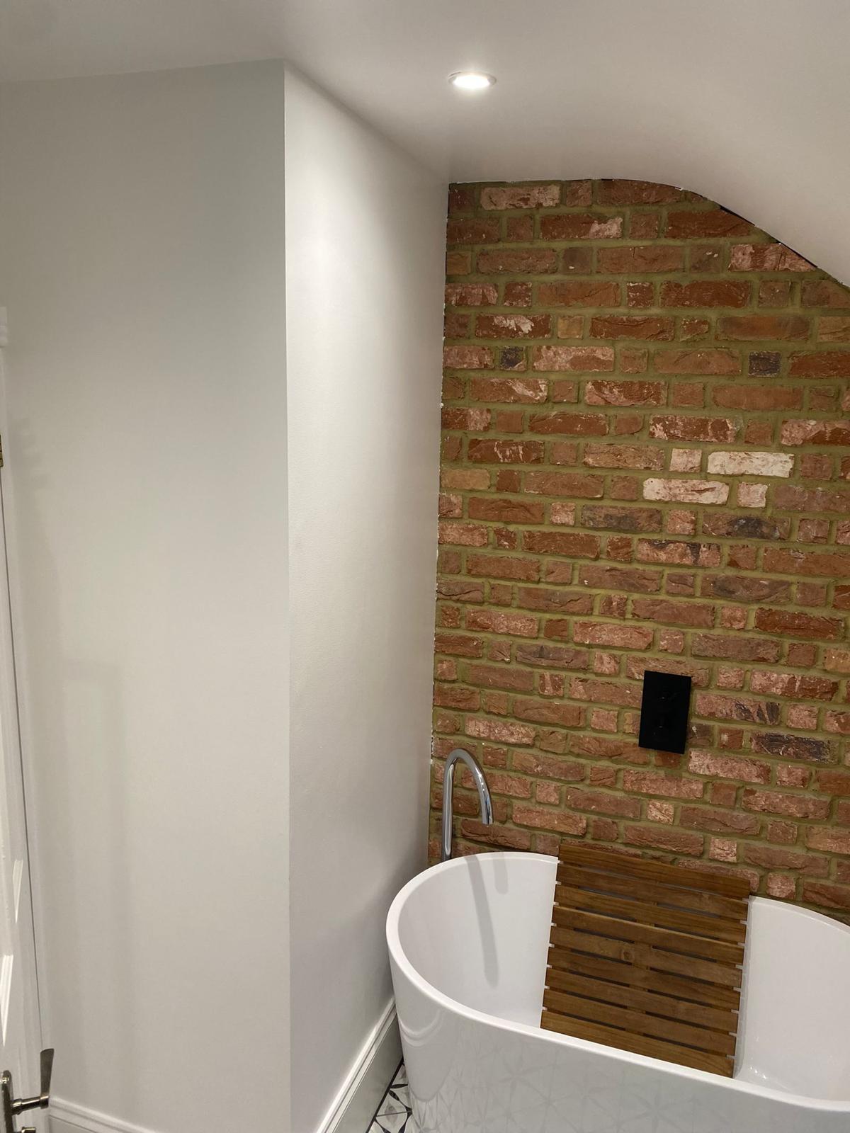 White freestanding bath beside an exposed brick feature wall