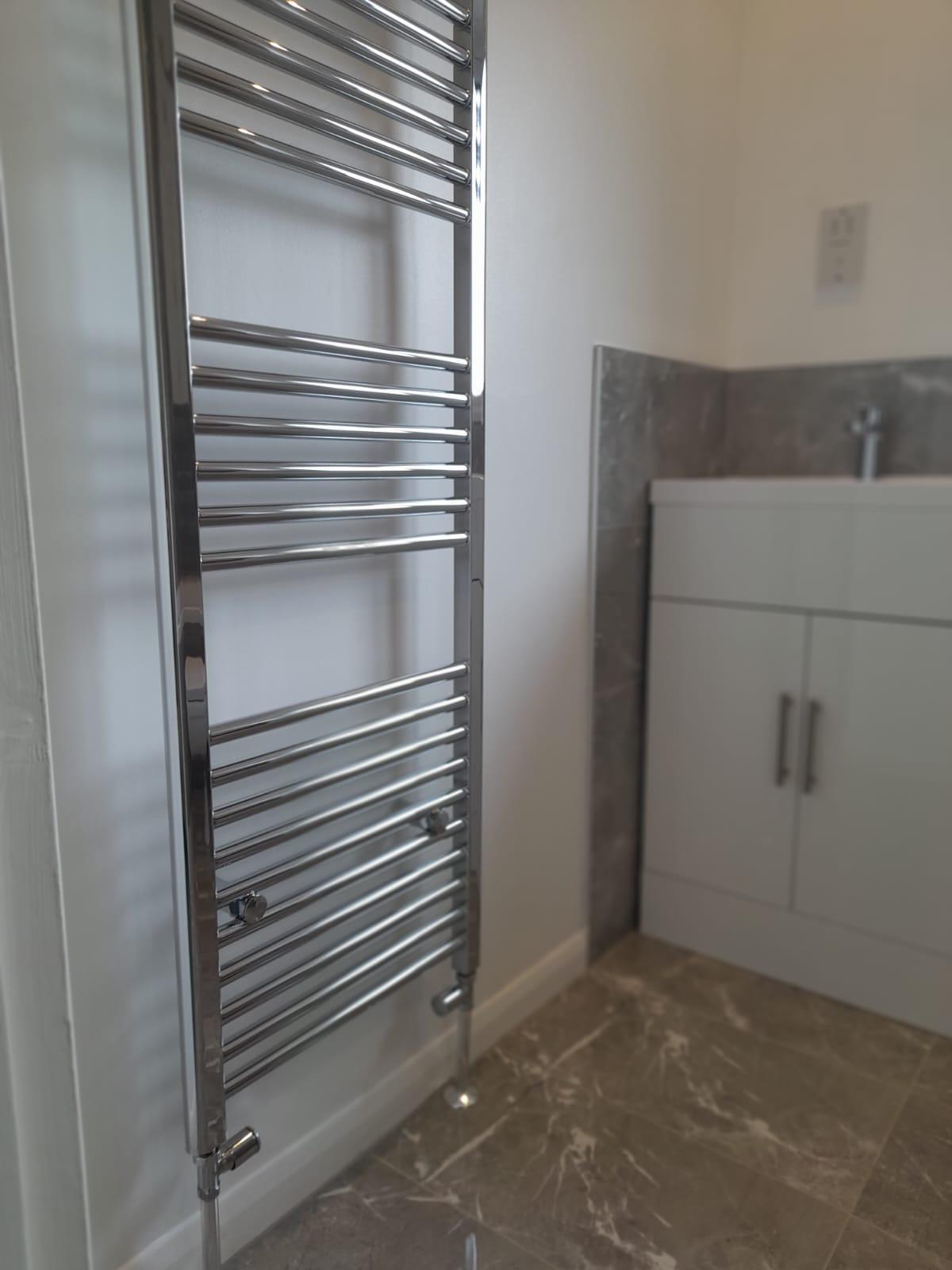 Tall chrome towel radiator beside a white bathroom vanity