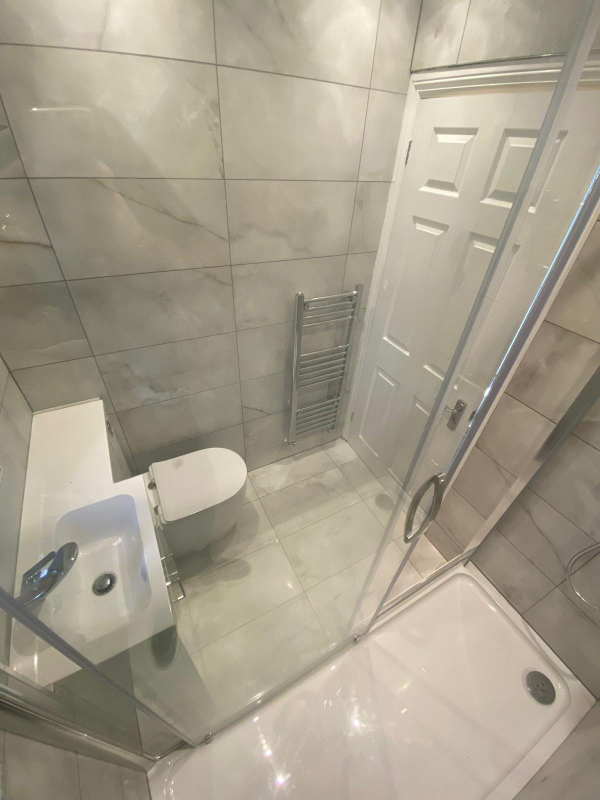 Compact shower room with glass enclosure, basin, WC and pale marble-effect tiles