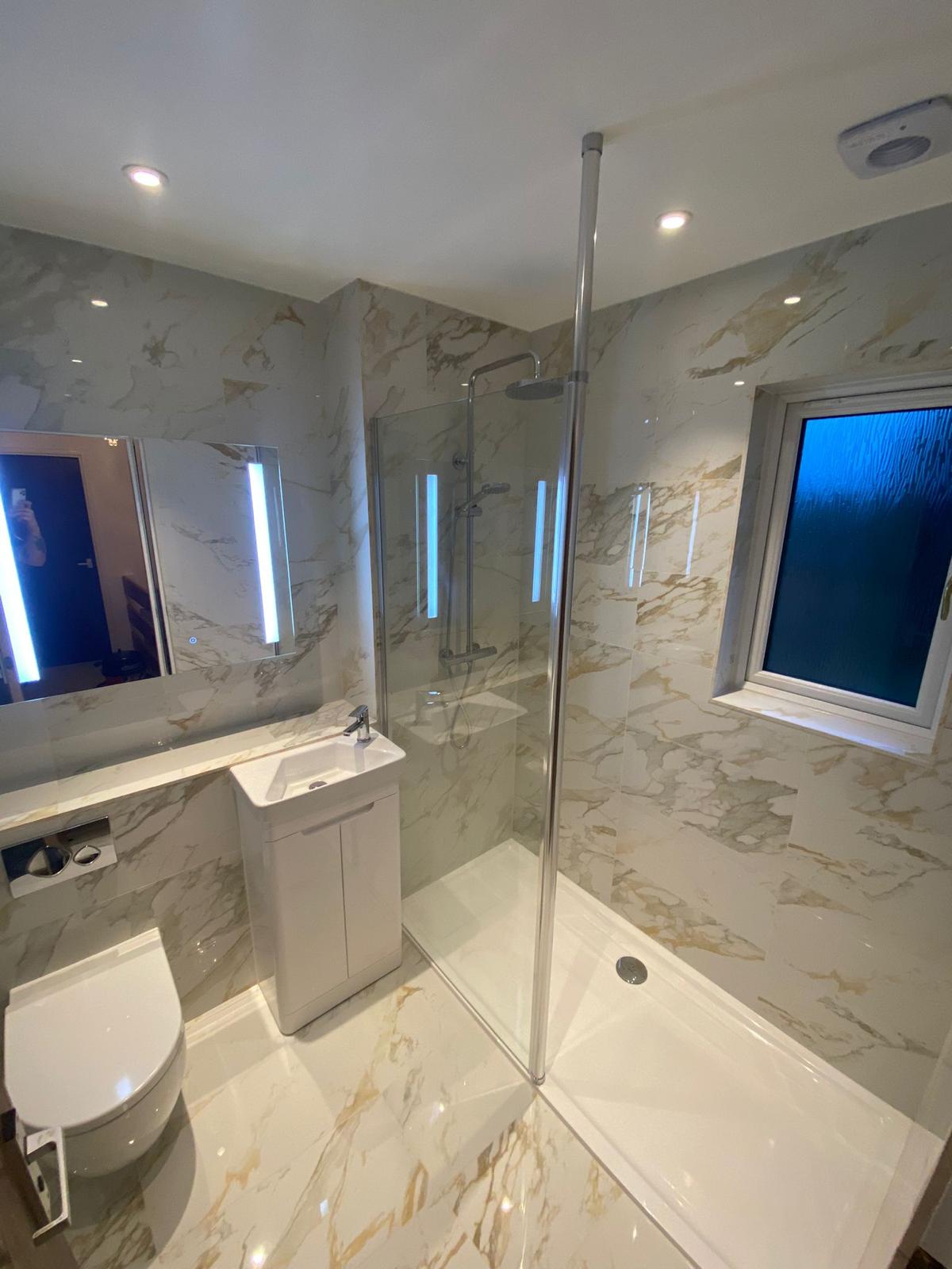 White and gold marble-effect shower room with glass enclosure and illuminated mirror