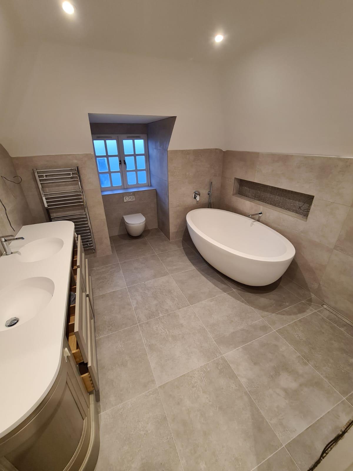 Freestanding oval bath in a pale marble-effect tiled bathroom