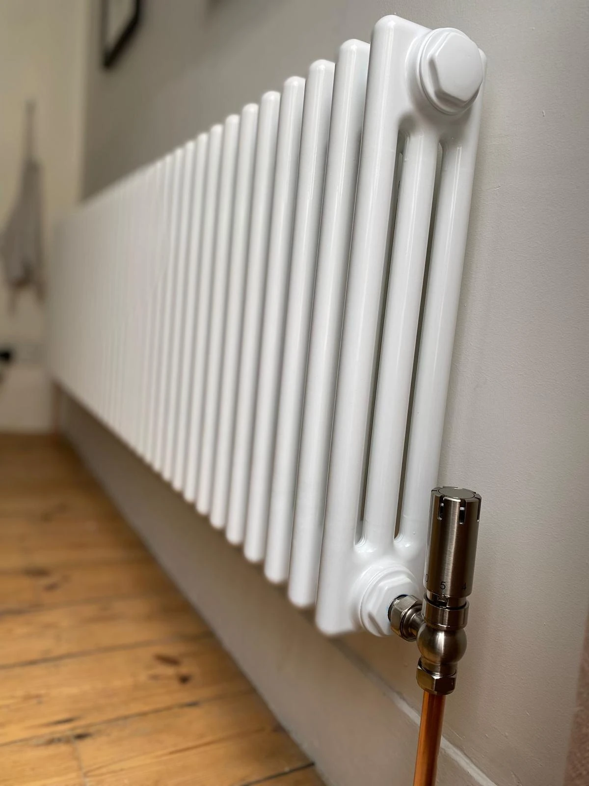 White column radiator with brushed-metal thermostatic valve and wooden floor