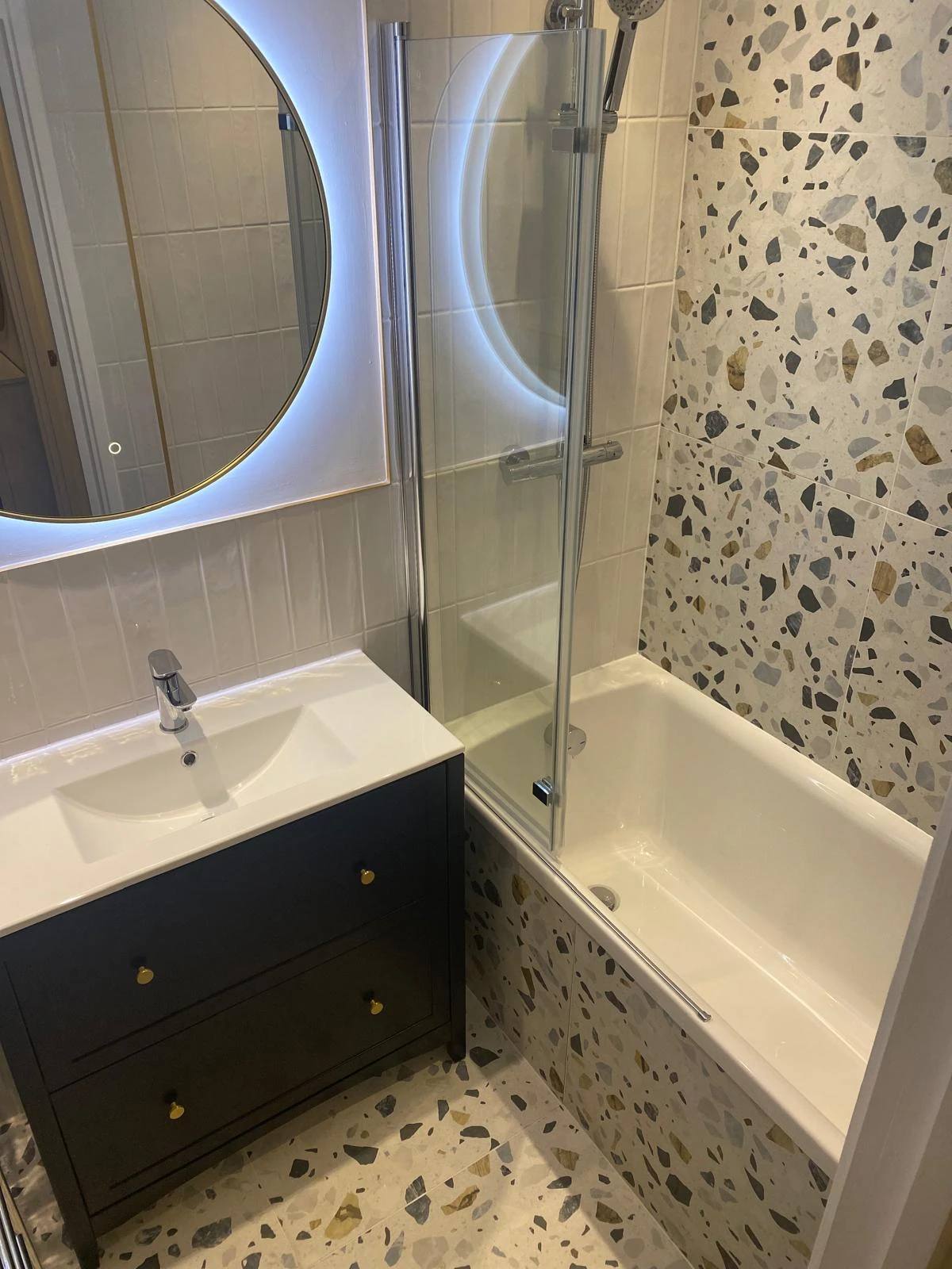 Terrazzo bathroom with navy vanity, round illuminated mirror and glazed bath screen