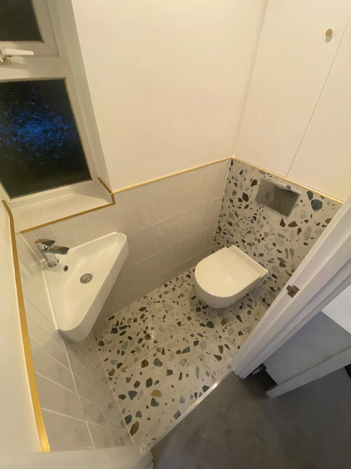 Wall-hung toilet and basin in a terrazzo cloakroom with gold trim